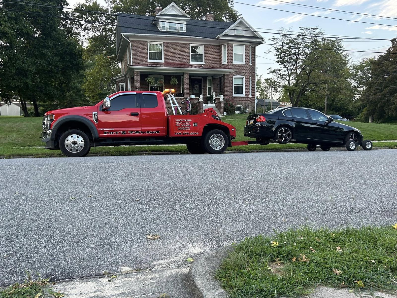 Red Pat's Towing truck towing a BMW on a residential street