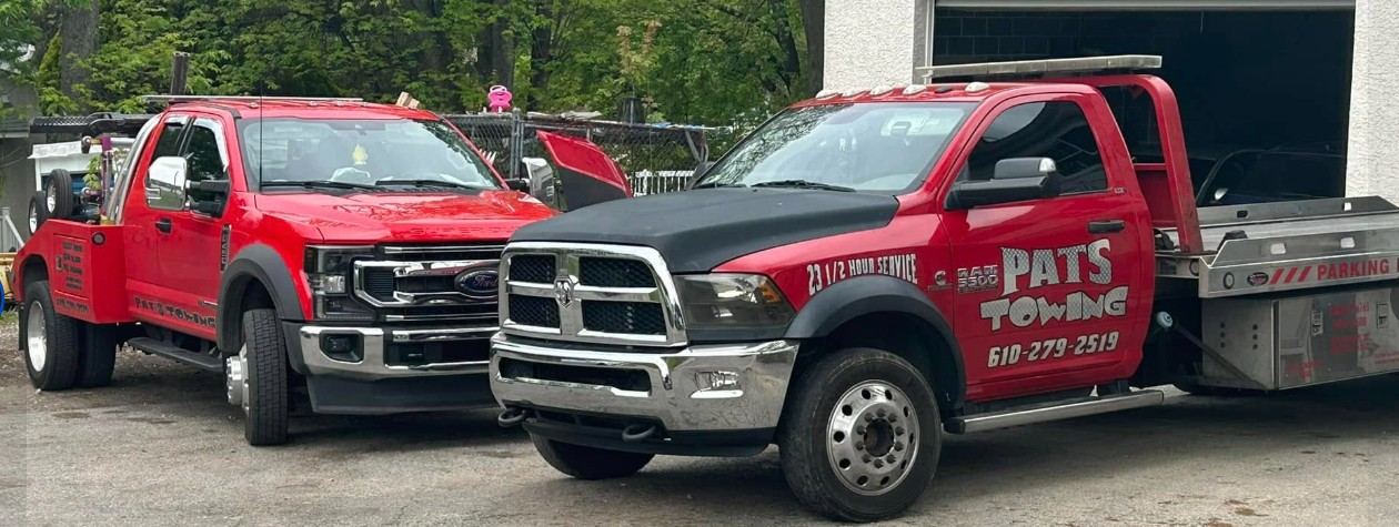 Two red Pat's Towing wrecker trucks side by side